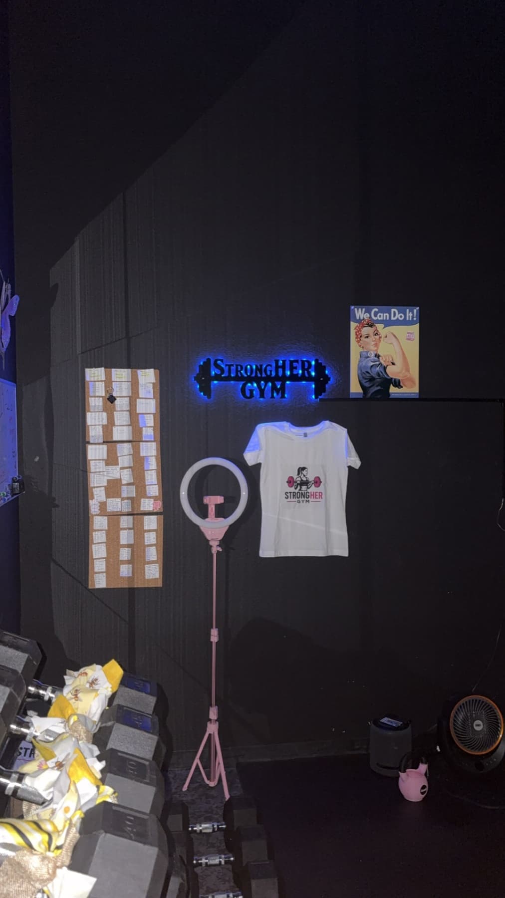 StrongHER Gym wall with its illuminated sign, client notes, and gym apparel